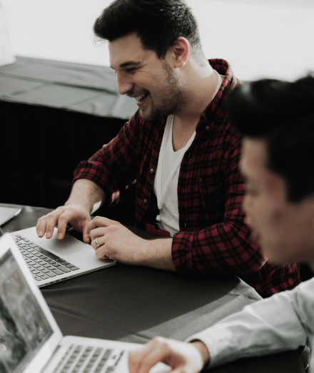 two men smiling while working on laptops